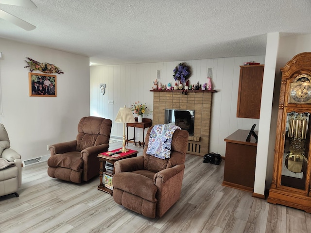 living room featuring a textured ceiling, visible vents, baseboards, light wood-type flooring, and a brick fireplace