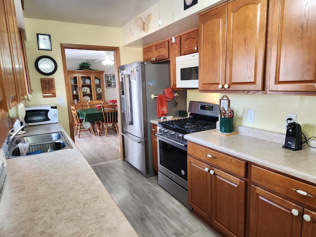 kitchen with light countertops, appliances with stainless steel finishes, a sink, and brown cabinets