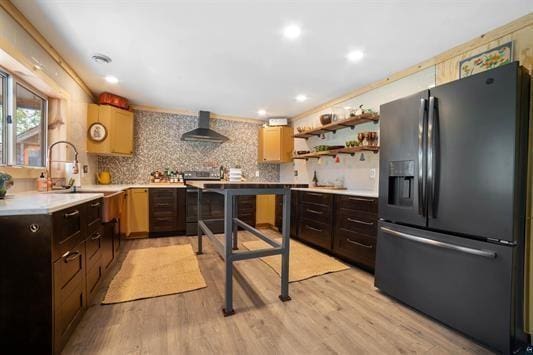 kitchen featuring range with electric cooktop, wall chimney exhaust hood, light countertops, light wood-style floors, and black fridge