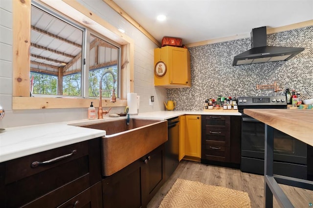 kitchen featuring light countertops, stainless steel electric range oven, wall chimney range hood, and a sink