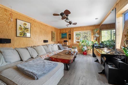 living area featuring ceiling fan, wood walls, and wood finished floors