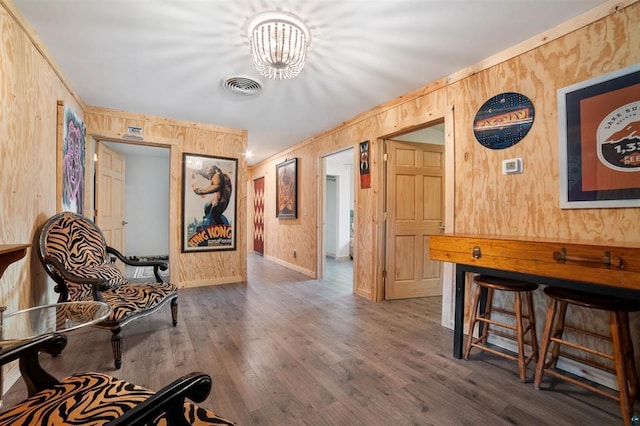 living area with a chandelier, wooden walls, wood finished floors, visible vents, and baseboards