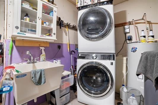 laundry area featuring water heater, laundry area, stacked washing maching and dryer, and a sink