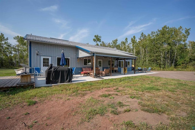 rear view of property with a patio area, an outdoor living space with a fire pit, metal roof, and a lawn