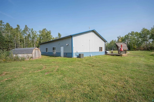 back of house featuring central air condition unit, a storage shed, a lawn, and an outbuilding