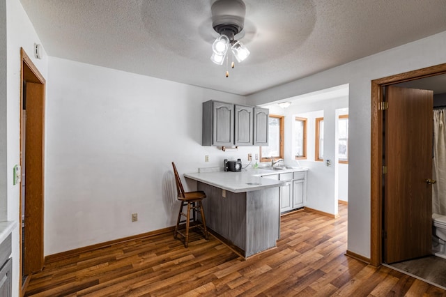 kitchen with gray cabinetry, light countertops, a kitchen bar, a peninsula, and wood finished floors