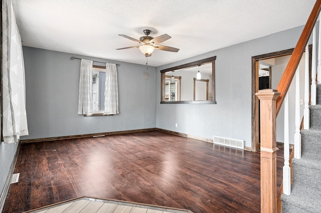 spare room with visible vents, a ceiling fan, wood finished floors, baseboards, and stairs