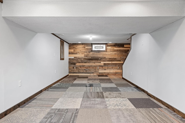 finished below grade area with wood walls, a textured ceiling, baseboards, and carpet floors