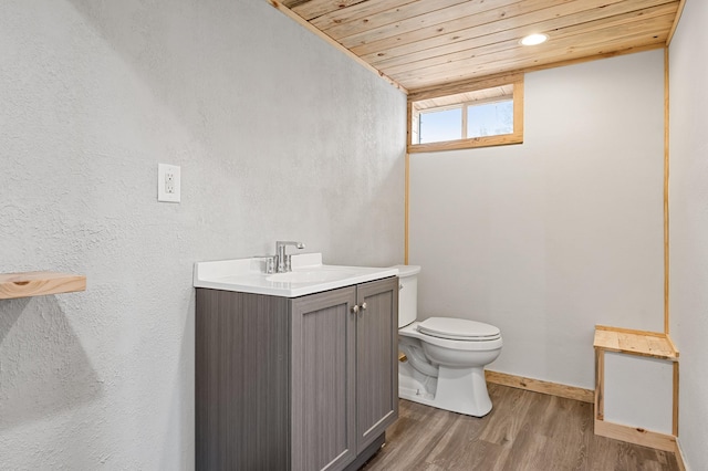 half bathroom featuring toilet, wood finished floors, wooden ceiling, vanity, and a textured wall