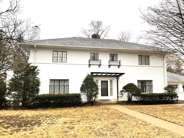 view of front of house featuring stucco siding, a balcony, and a chimney