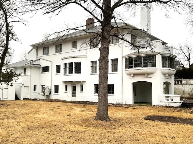 back of house with stucco siding and a chimney