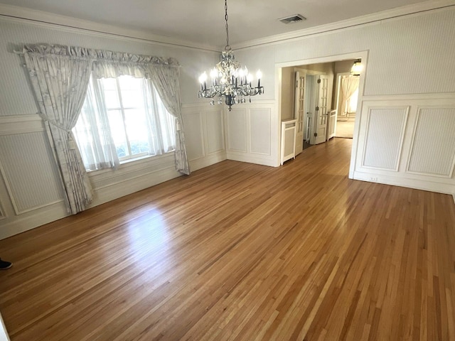 unfurnished dining area with light wood finished floors, visible vents, a chandelier, and a decorative wall