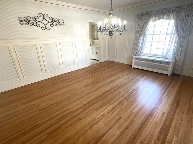 unfurnished dining area with a notable chandelier, a decorative wall, radiator heating unit, and wood finished floors