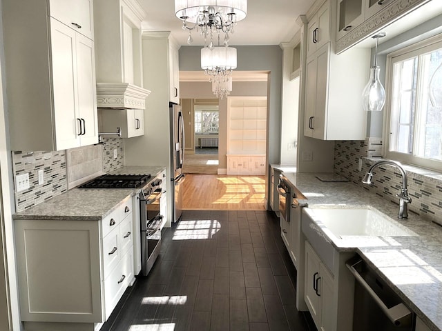 kitchen with custom range hood, a sink, light stone counters, stainless steel appliances, and a chandelier