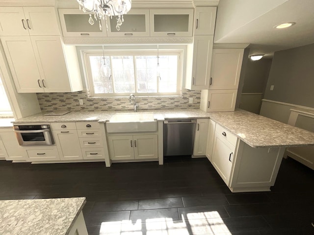 kitchen with decorative backsplash, appliances with stainless steel finishes, glass insert cabinets, and a peninsula