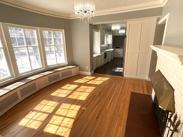 unfurnished dining area with crown molding, a chandelier, baseboard heating, wood finished floors, and a textured ceiling