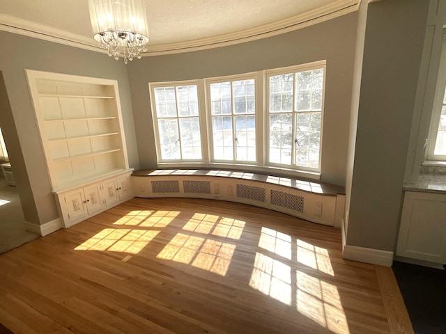 unfurnished dining area with a notable chandelier, built in features, wood finished floors, crown molding, and baseboards