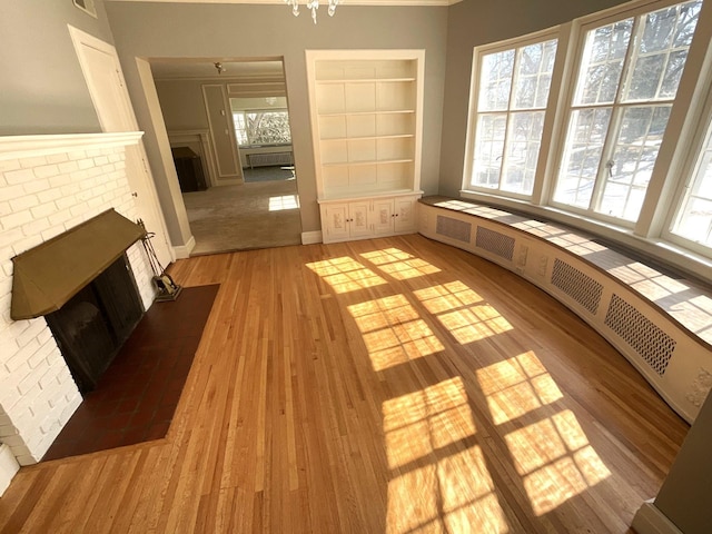 unfurnished living room with radiator, a brick fireplace, built in shelves, and light wood-style floors