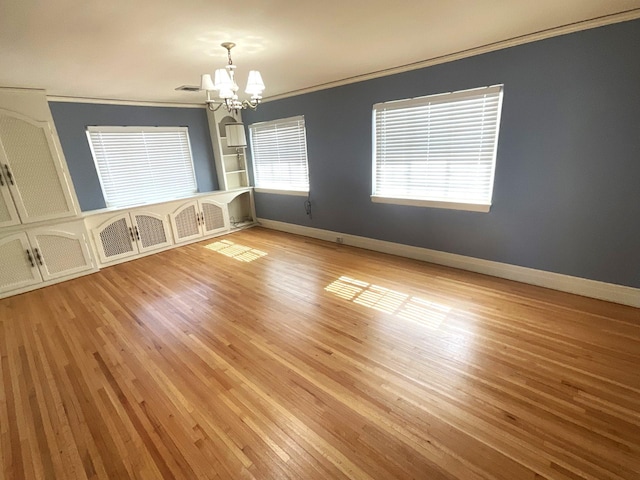 empty room featuring a chandelier, light wood-style flooring, baseboards, and ornamental molding