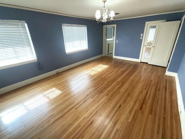 spare room with baseboards, a notable chandelier, wood finished floors, and crown molding