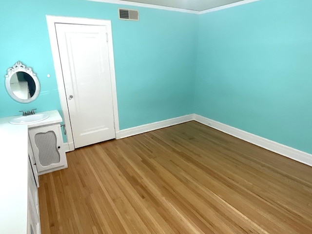 unfurnished room featuring wood finished floors, baseboards, visible vents, a sink, and crown molding