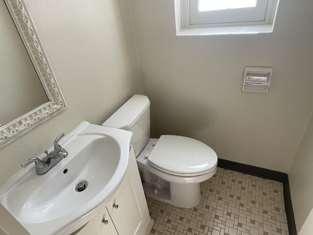 half bath featuring vanity, toilet, and baseboards