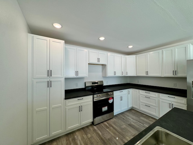 kitchen featuring appliances with stainless steel finishes, dark countertops, white cabinetry, and wood finished floors