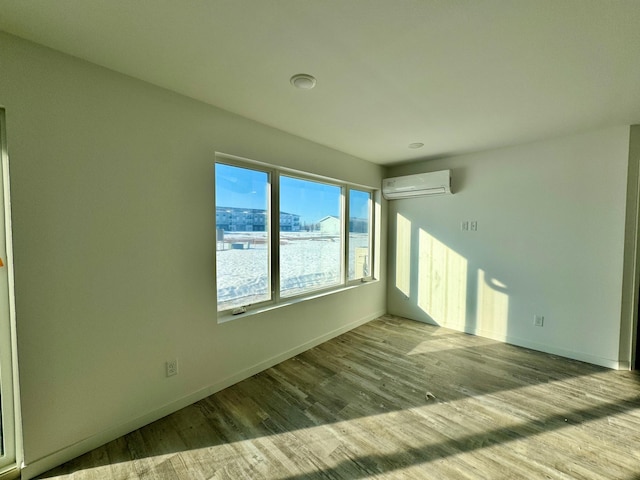 spare room featuring an AC wall unit, baseboards, and wood finished floors