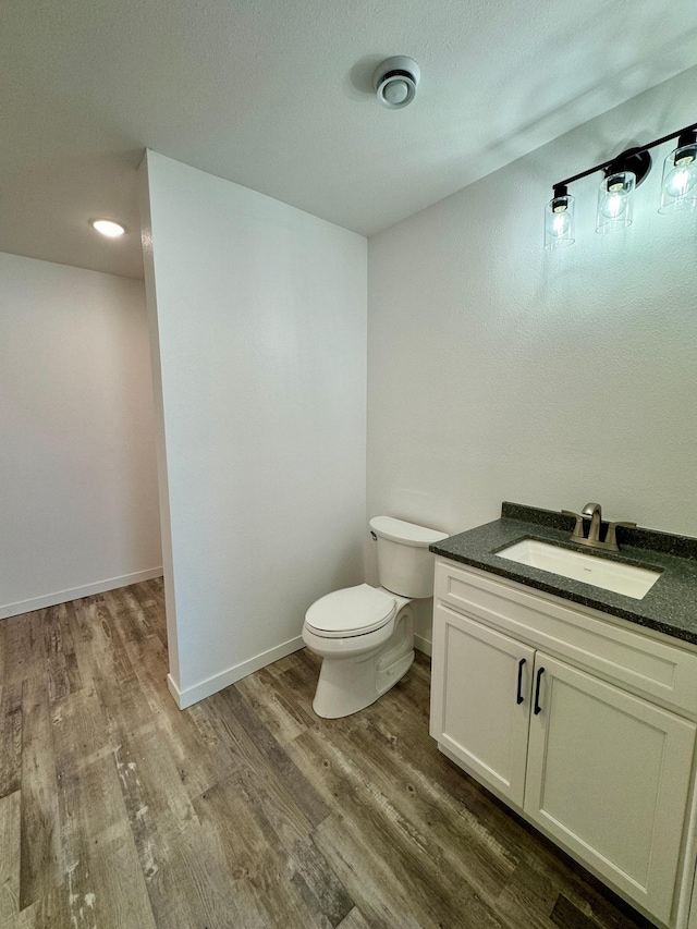 half bath featuring toilet, baseboards, wood finished floors, and vanity