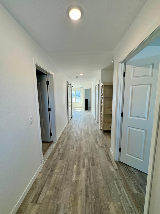 corridor featuring wood finished floors, baseboards, and a barn door