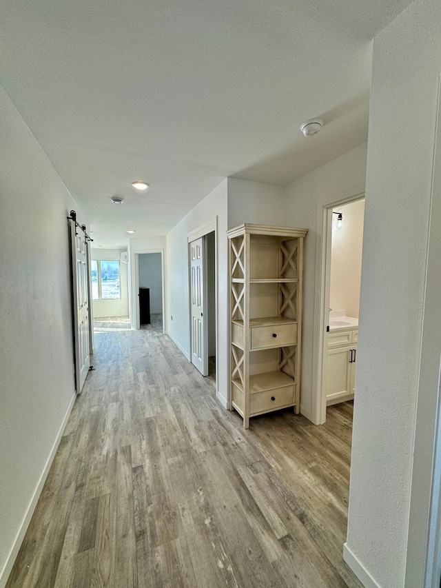 hallway with light wood-style floors, a barn door, and baseboards