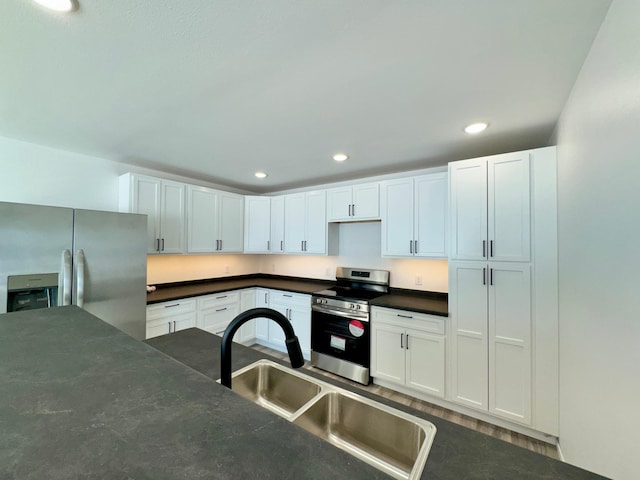 kitchen featuring dark countertops, recessed lighting, appliances with stainless steel finishes, white cabinetry, and a sink