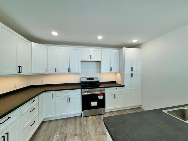 kitchen featuring electric range, dark countertops, white cabinetry, and light wood-style floors