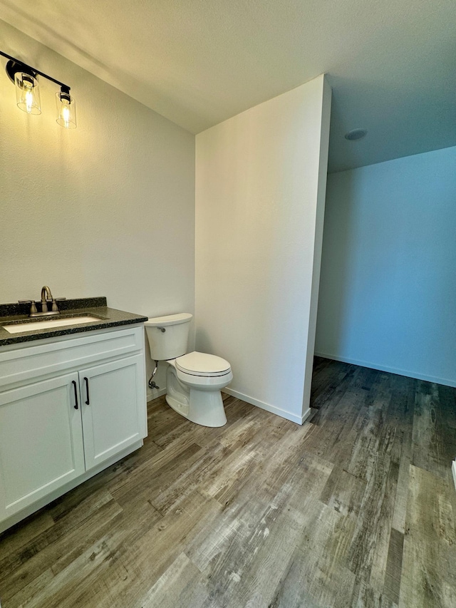 bathroom with baseboards, vanity, toilet, and wood finished floors