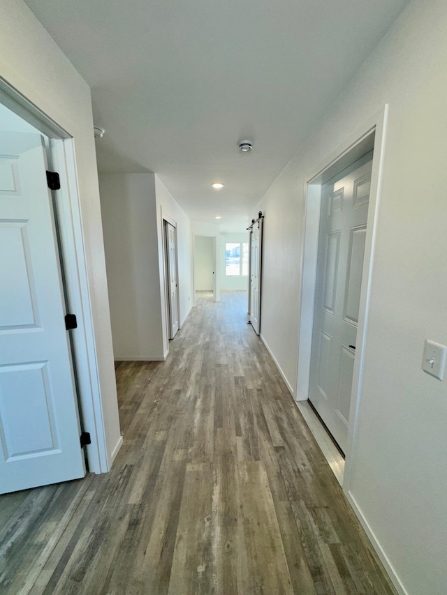 hallway featuring a barn door, wood finished floors, and baseboards