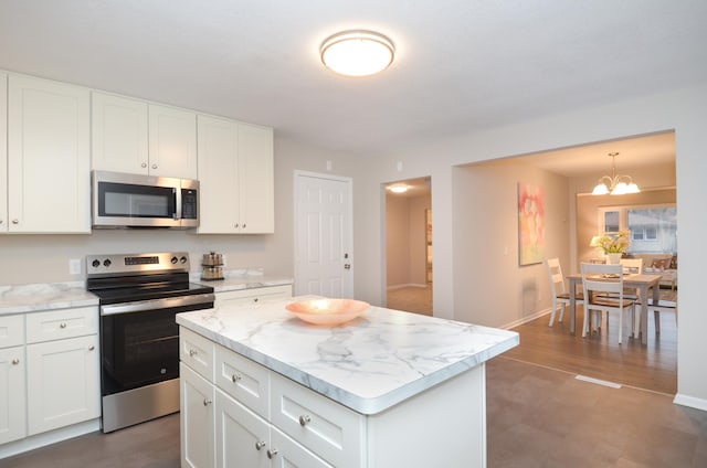 kitchen featuring light stone counters, stainless steel appliances, white cabinets, a center island, and an inviting chandelier