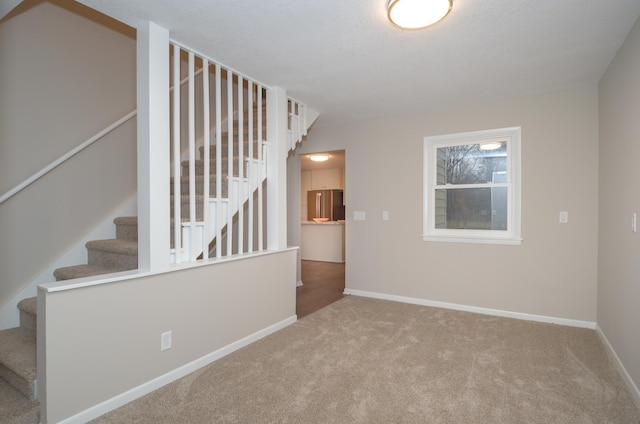 carpeted spare room with baseboards and stairway