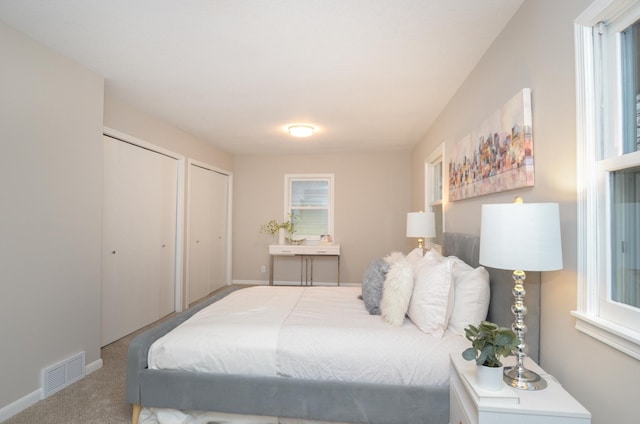 bedroom with carpet floors, baseboards, visible vents, and multiple closets