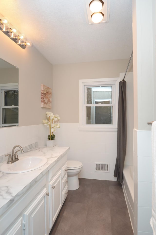 full bath with a wainscoted wall, tile walls, visible vents, toilet, and vanity