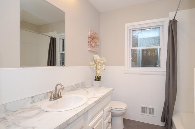 bathroom featuring visible vents, wainscoting, toilet, vanity, and tile walls