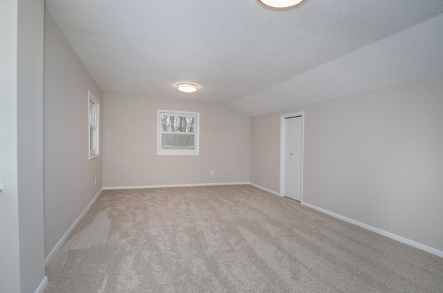 empty room with lofted ceiling, a textured ceiling, baseboards, and light colored carpet