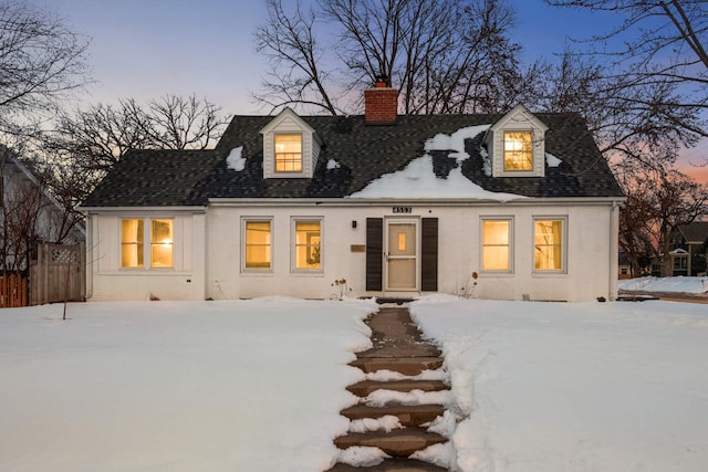 cape cod home featuring a shingled roof, a chimney, fence, and brick siding