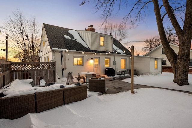 snow covered rear of property with brick siding, outdoor lounge area, fence, a chimney, and a patio area