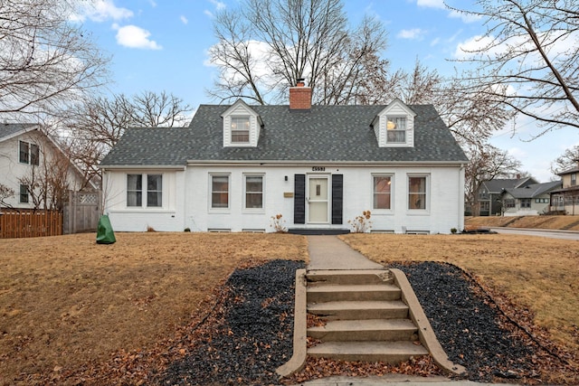 cape cod-style house featuring roof with shingles, brick siding, a chimney, and fence