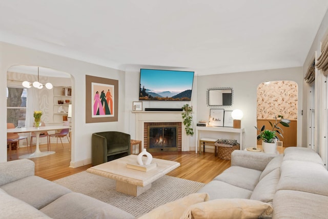 living area featuring a chandelier, arched walkways, a fireplace, and wood finished floors