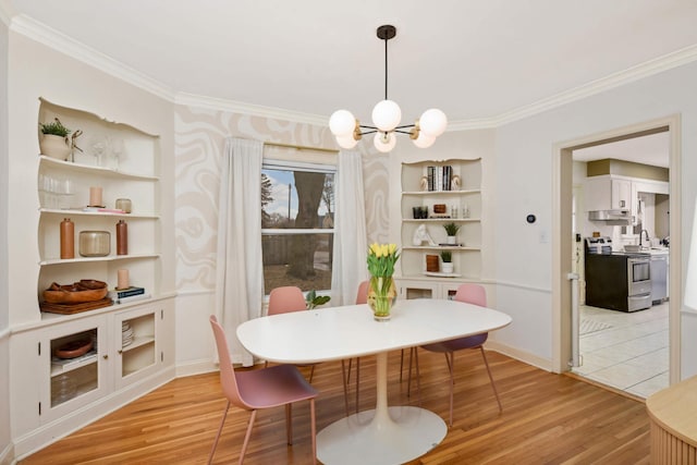 dining room with light wood-type flooring, built in shelves, ornamental molding, and a notable chandelier