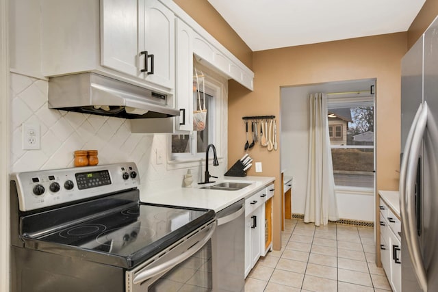 kitchen with light tile patterned floors, under cabinet range hood, stainless steel appliances, a sink, and white cabinets