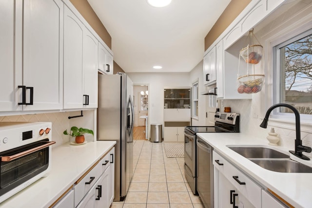 kitchen featuring light tile patterned floors, appliances with stainless steel finishes, a sink, and white cabinetry