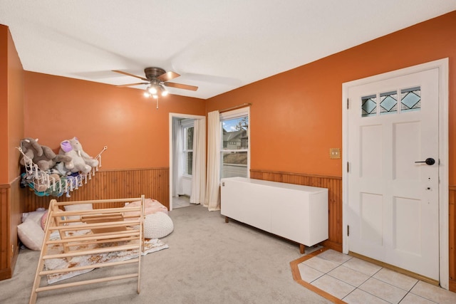 foyer featuring a wainscoted wall, carpet, a ceiling fan, and wood walls