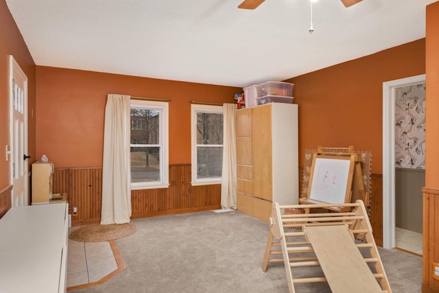 interior space with ceiling fan, wood walls, wainscoting, and carpet flooring